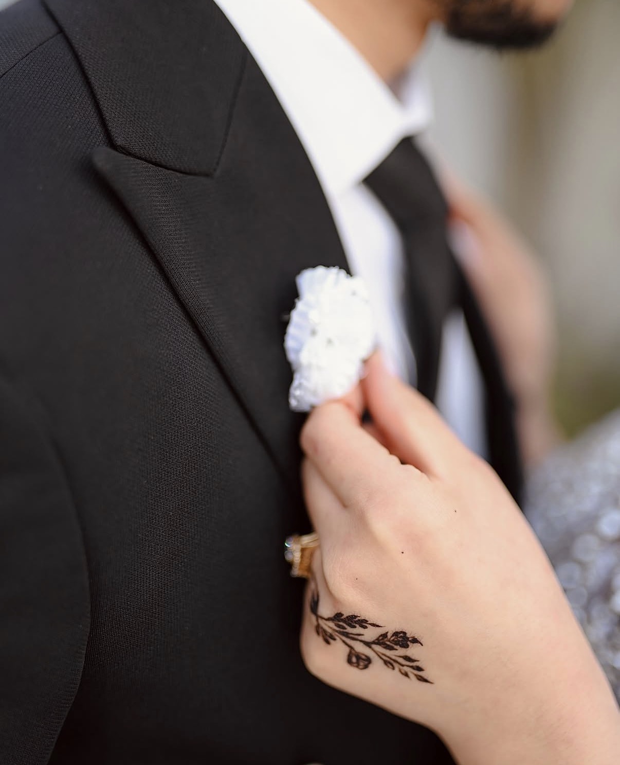 La mariée ajuste la boutonnière du marié, motif de henné sur sa main